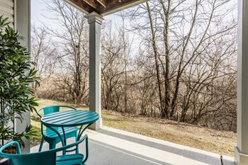 A green table and chairs on a porch with trees in the background.